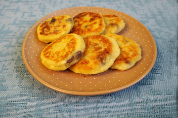 six yellow sugar-free cheesecakes with banana and raisins in cornmeal lie in a brown round plate with polka dots on a blue textured background side view . cooking cheesecakes at home