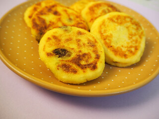 six yellow sugar-free cheesecakes with banana and raisins in cornmeal lie in a brown round plate with polka dots on a pink background side view . cooking cheesecakes at home