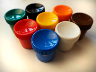 blue red yellow white green black orange brown plastic closed jars with gouache on a gray background side view