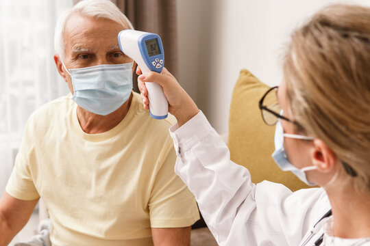 Doctor checking body temperature to elderly man during home visit