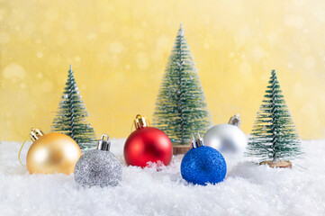 Naklejka na ściany i meble Colorful christmas balls in the snow among the toy christmas trees. Bokeh with lights. Beautiful Christmas card.