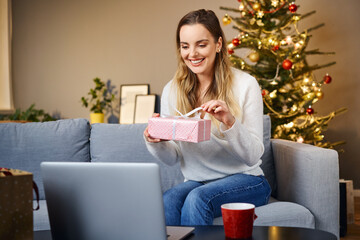 Woman opening christmas present during video call with family. Social distancing concept