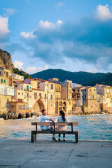 couple on vacation Sicily visiting the old town of Cefalu,sunset at the beach of Cefalu Sicily, old...