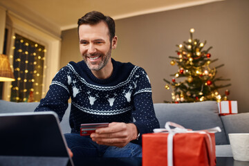 Happy man doing Christmas shopping online with tablet and credit card