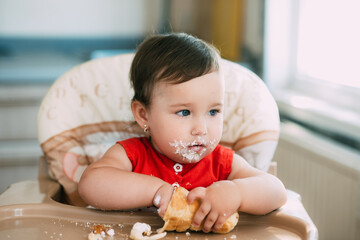 baby girl in the kitchen eating tubes with custard or protein cream