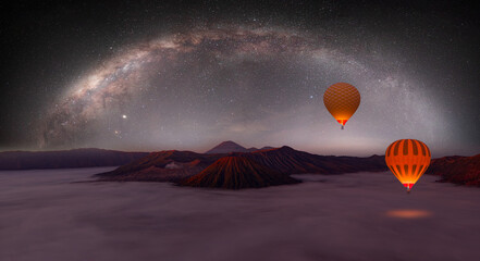 Hot air balloon is flying above the clouds - Beautiful night landscape with silhouette of Bromo mountain on the background Milky way galaxy - Bromo Tengger Semeru National Park , Indonesia