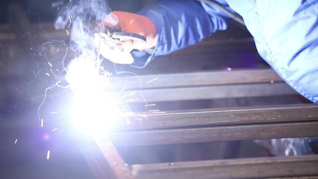 Factory worker welds metal. Welding with electrode using a welder machine.Sparks and flashes fly
