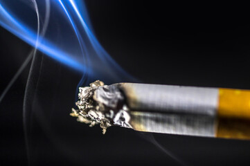 Qualmende Zigarette mit Asche vor schwarzem Hintergrund