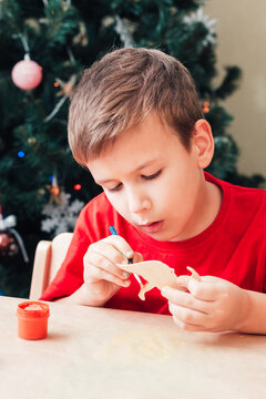 Cute 7 years old child boy paints wooden dinosaur toy for Christmas tree