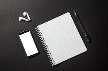 Subjects for a business conference or online lesson on a black background. Items are stacked diagonally. Open notebook, pen, smartphone with blank white display for your advertising. View from above.