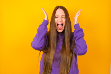 Young beautiful Caucasian woman wearing purple sweater against yellow wall goes crazy as head goes...