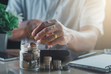 Obraz na płótnie Canvas Man's hand taking the coin put in a glass jar, coin pile, calculator, money-saving concept