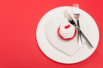 top view of cupcake on plate with cutlery on red background