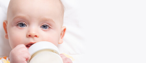 Banner format. Caucasian infant with baby milk bottle. Close up. Copy space. Focus on babies eyes. Artificial feeding. Baby milk formula.