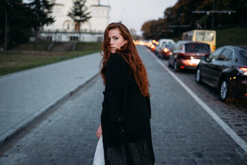 red-haired young woman in autumn runs down the street with cars
