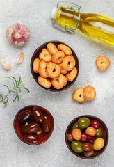 Tarallini-traditional Italian small bagels. Taralli. Tasty snack. Black and green olives, Kalamata, olive oil, garlic and rosemary on a grey concrete background. Selective focus