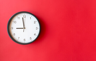 Round wall clock on red surface showing 9 o’clock, layout, top view, place for text.