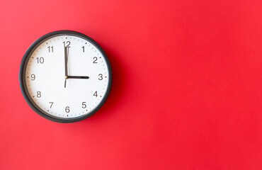 Round wall clock on red surface showing 3 o’clock, layout, top view, place for text.