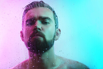 Portrait of handsome man through wet glass in neon light