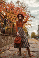  Outdoor autumn fashion full-length portrait: elegant woman wearing stylish orange hat, turtleneck,...
