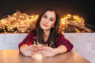 
the girl celebrates the new year and christmas indoors against the background of a Christmas tree of garlands, Christmas decorations and lanterns