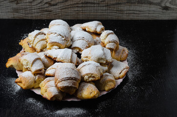 Homemade cookies in the form of bagels with jam filling sprinkled with powdered sugar on a wooden background.