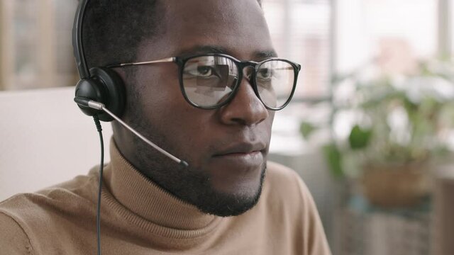 Close up of young African-American male call center worker wearing headset sitting at workplace and receiving phone call from client