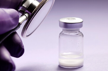 stethoscope and vaccine in doctor hand holding vaccine in glass vial with lilac and black background