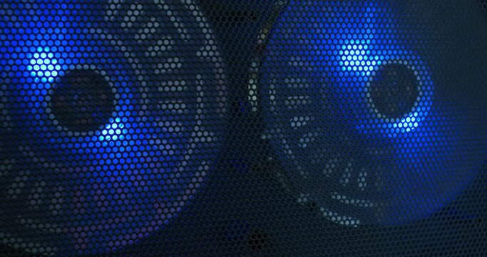 Computer cooling fans illuminated by blue led lights spinning behind black wire mesh macro close up shot shallow depth of field
