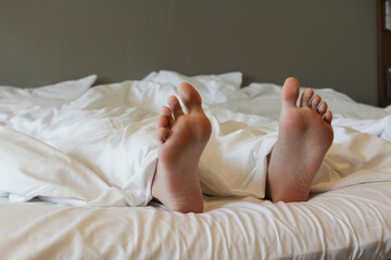 Legs of a young woman lying under a white blanket