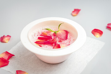 A white bowl of water with pink rose petals on a white table in the spa salon