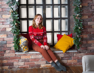 A blonde girl in a red sweater sits on the windowsill.