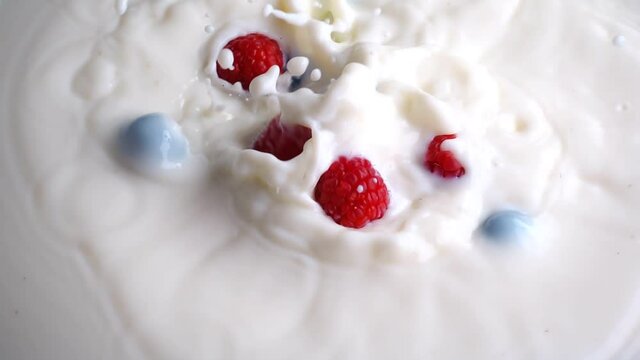 Blueberries and raspberries falling into milk in slow motion