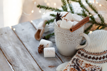 Winter hot drink. Cozy home composition with white mug with chocolate and marshmallow, cinnamon. Knitted mittens, christmas lights, wooden background. Festive holiday atmosphere, family spirit. Close