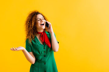 amazed young woman talking on smartphone isolated on yellow