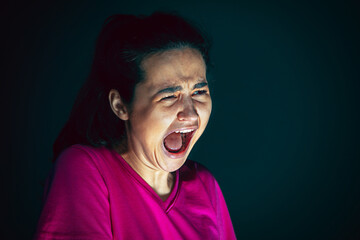 Fototapeta premium Screaming. Portrait of young crazy scared and shocked caucasian woman isolated on dark background. Copyspace for ad. Bright facial expression, human emotions concept. Looking horror on TV, cinema.