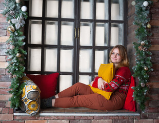 A blonde girl in a red sweater sits on the windowsill.