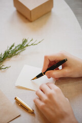 Female hands writing Christmas card on wooden table.