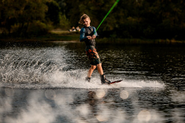 Fototapeta premium active young man in wetsuit and vest rides wakeboard on the river