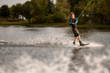 view on young man in wetsuit and vest riding wakeboard on the river