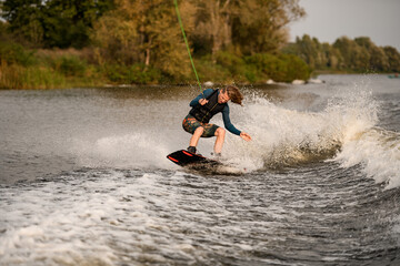 handsome young man stands with bent knees on wakeboard and ride down on wave