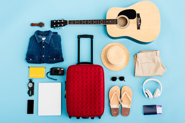 top view of sunglasses, clothing, accessories and devices near red luggage on blue