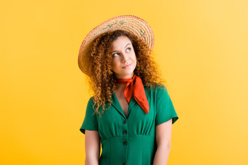 pensive young woman in green dress and straw hat looking away on yellow