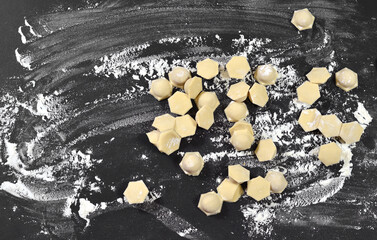 Dumplings, ravioli on a black table sprinkled with wheat flour. There are many small pieces of...