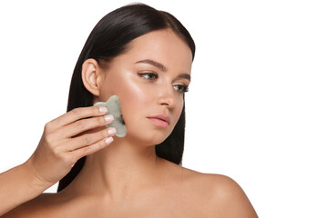 Obraz na płótnie Canvas Beautiful girl with natural makeup and clean skin. Holds in hand a jade face scrubber for slimming anti aging wrinkles. Massage instrument for body skin care. Detox facial massager