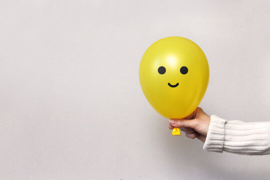 A Man Holds A Balloon With A Happy Face In His Hand. Joy, Smiles, Optimism In A Person's Life