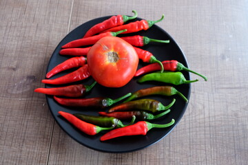 Red vegetables on a black plate. Organic tomatoes with peppers on wooden background. Summer or autumn concept. Natural food. It is called 