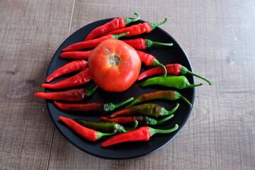 Red vegetables on a black plate. Organic tomatoes with peppers on wooden background. Summer or autumn concept. Natural food. It is called 