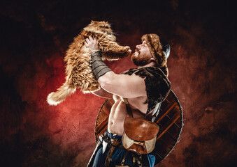 Portrait of joyful and muscular viking warrior with shield on his back he plays with his little...
