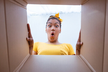Excited african woman unpacking carton box at home